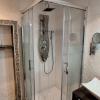 Reforma de baño en Madrid: ducha con mampara de cristal y columna de ducha, paredes alicatadas y marco de mosaico de piedra en el hueco.